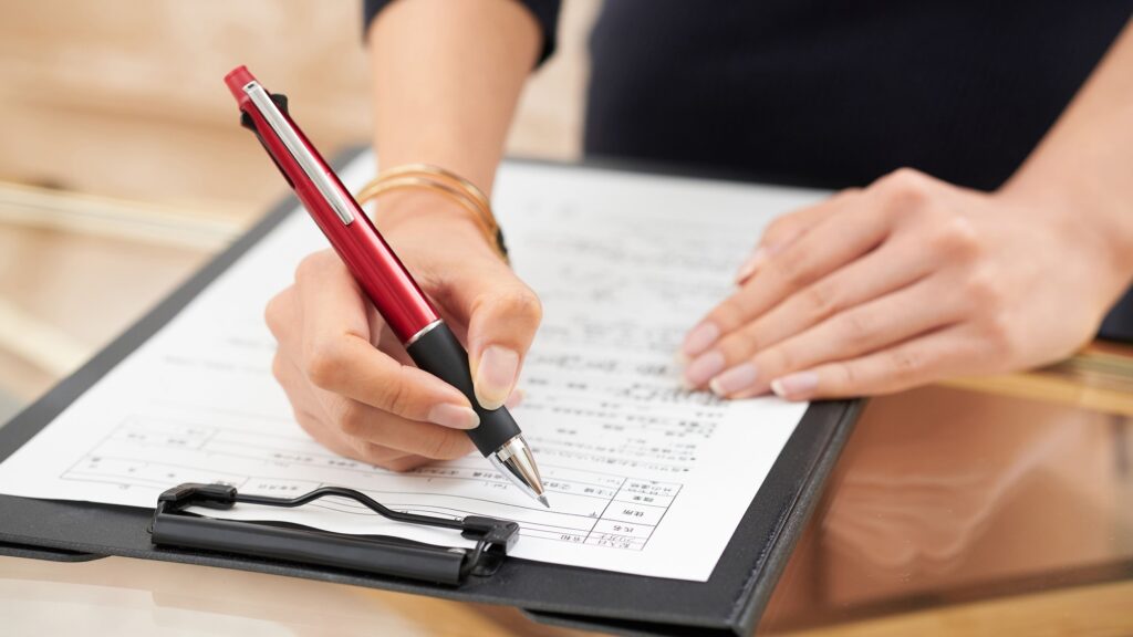 展示会で配られるアンケート用紙に記入する来場者。ボールペンを持ち、書類に書き込む手元の様子を撮影。